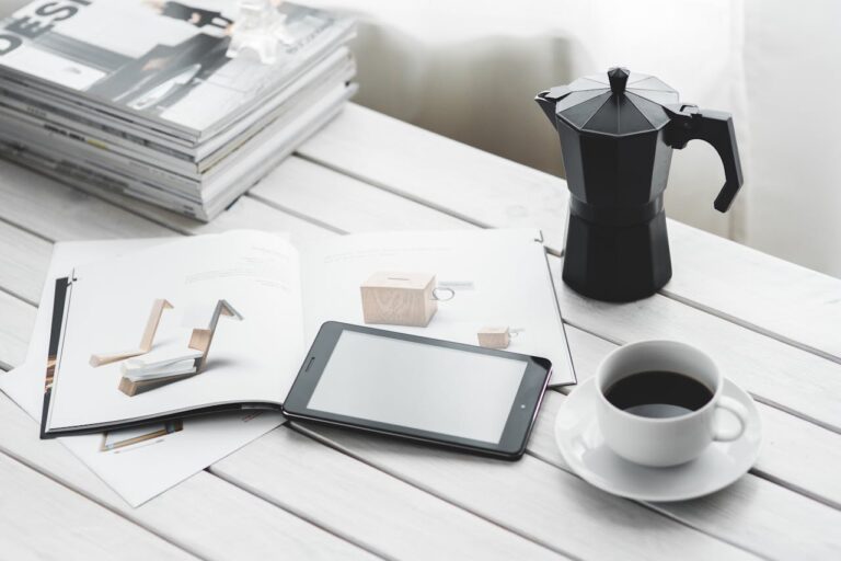 Stylish indoor workspace with a tablet, coffee cup, and magazines on a white table.