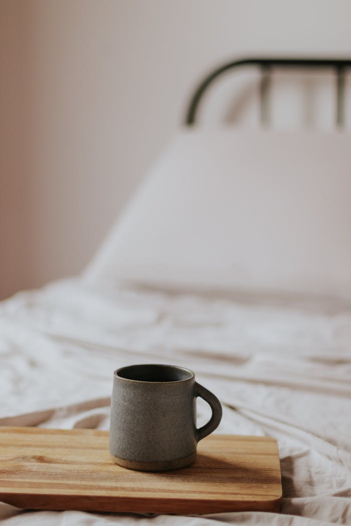 A warm ceramic mug on a wooden tray in a minimal bedroom setting, inviting a tranquil morning vibe.