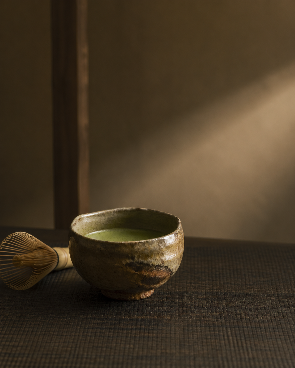 A single tea bowl resting on a dark lacquer mat, with a bamboo whisk laid beside it