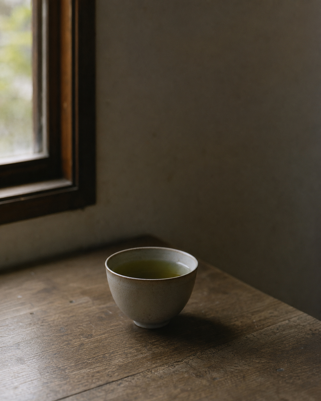 A plain ceramic cup of tea on a wooden surface beside a window with soft natural light