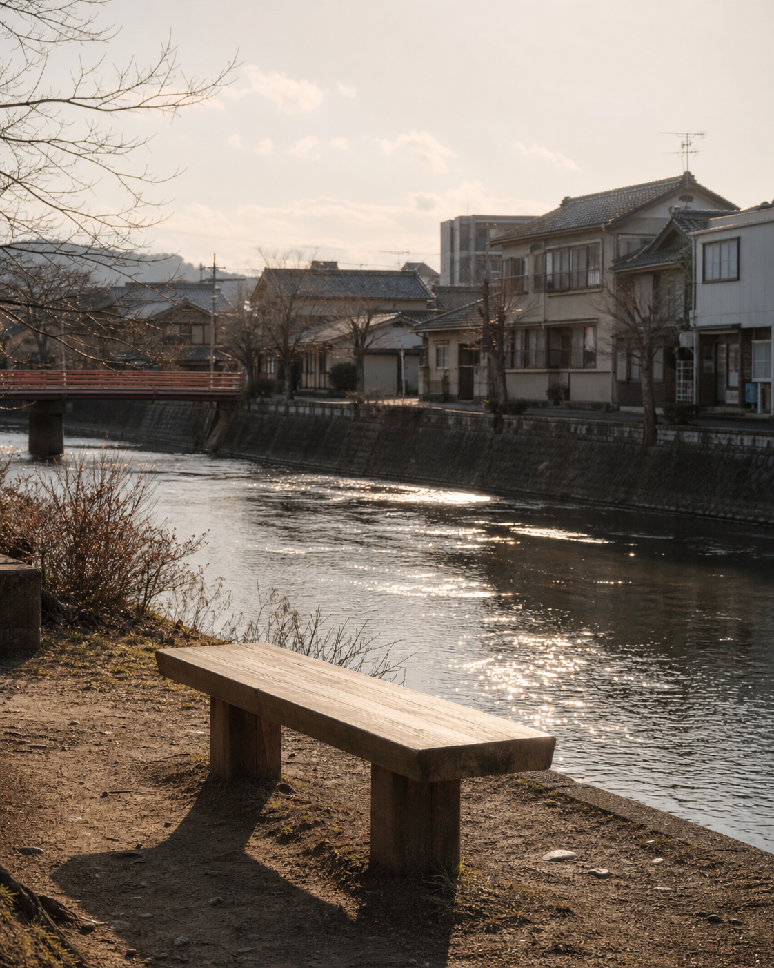 A wooden bench beside a small river in a quiet Japanese town, late afternoon light on the water