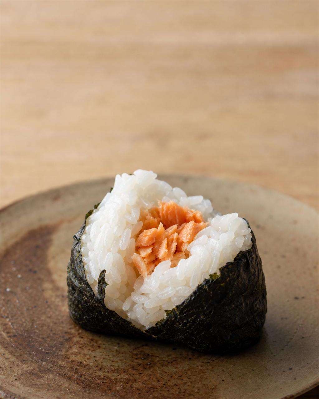 Salted salmon onigiri unwrapped on a wooden surface, flakes of pink salmon visible at the center
