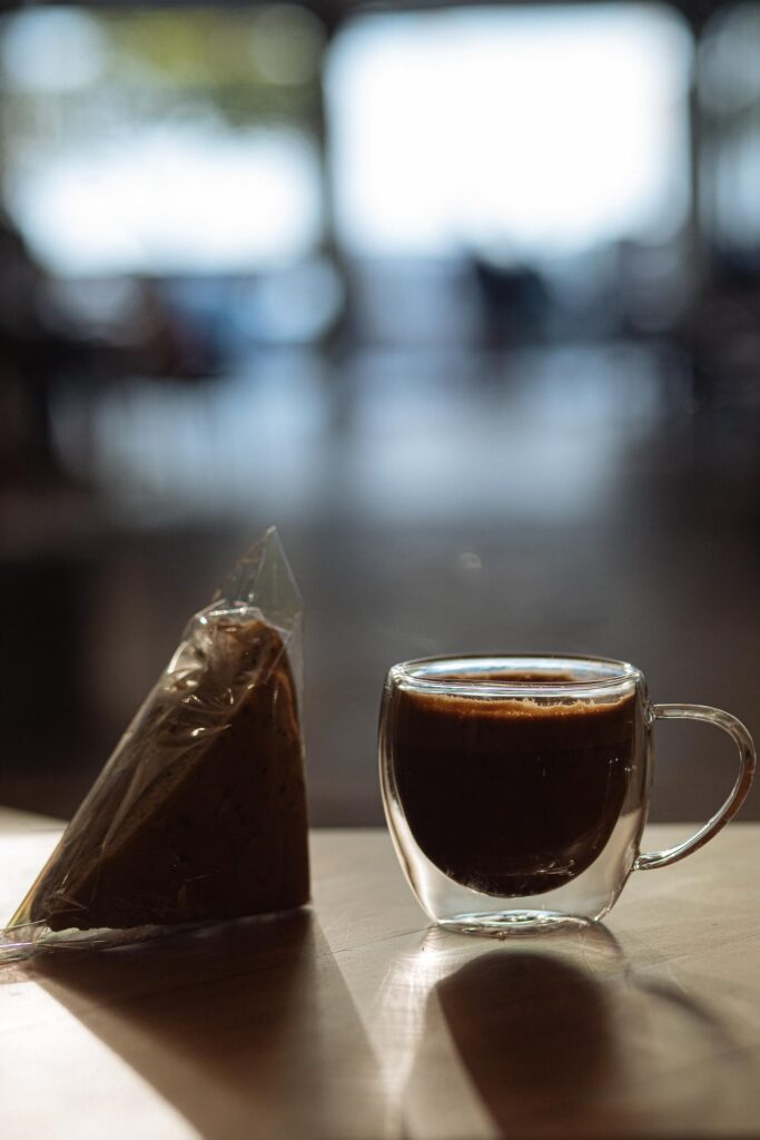 A stylish glass cup of coffee with a chocolate cake slice on a wooden table indoors.